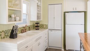A kitchen with white cabinets, a dishwasher, and a refrigerator. There are shelves with glassware and a knife block.