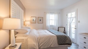 A bedroom with a bed, bedside lamps, a dresser, and a window with curtains.