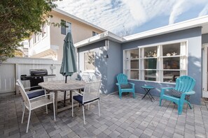 A patio with a table and chairs, a grill, and a blue chair with a cushion.