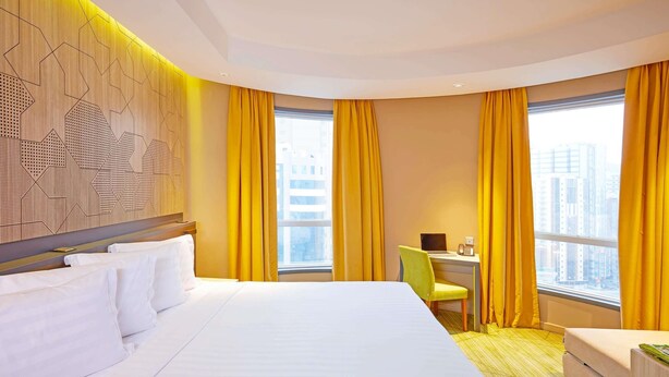 A hotel room with a large bed, a desk with a chair, and a view of the city through large windows. - ibis Styles Makkah (Makkah)
