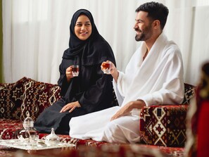 Ein Zimmer mit gestreiften Sofas, einem Tisch mit Teekanne und einer Person in weißer Kleidung.