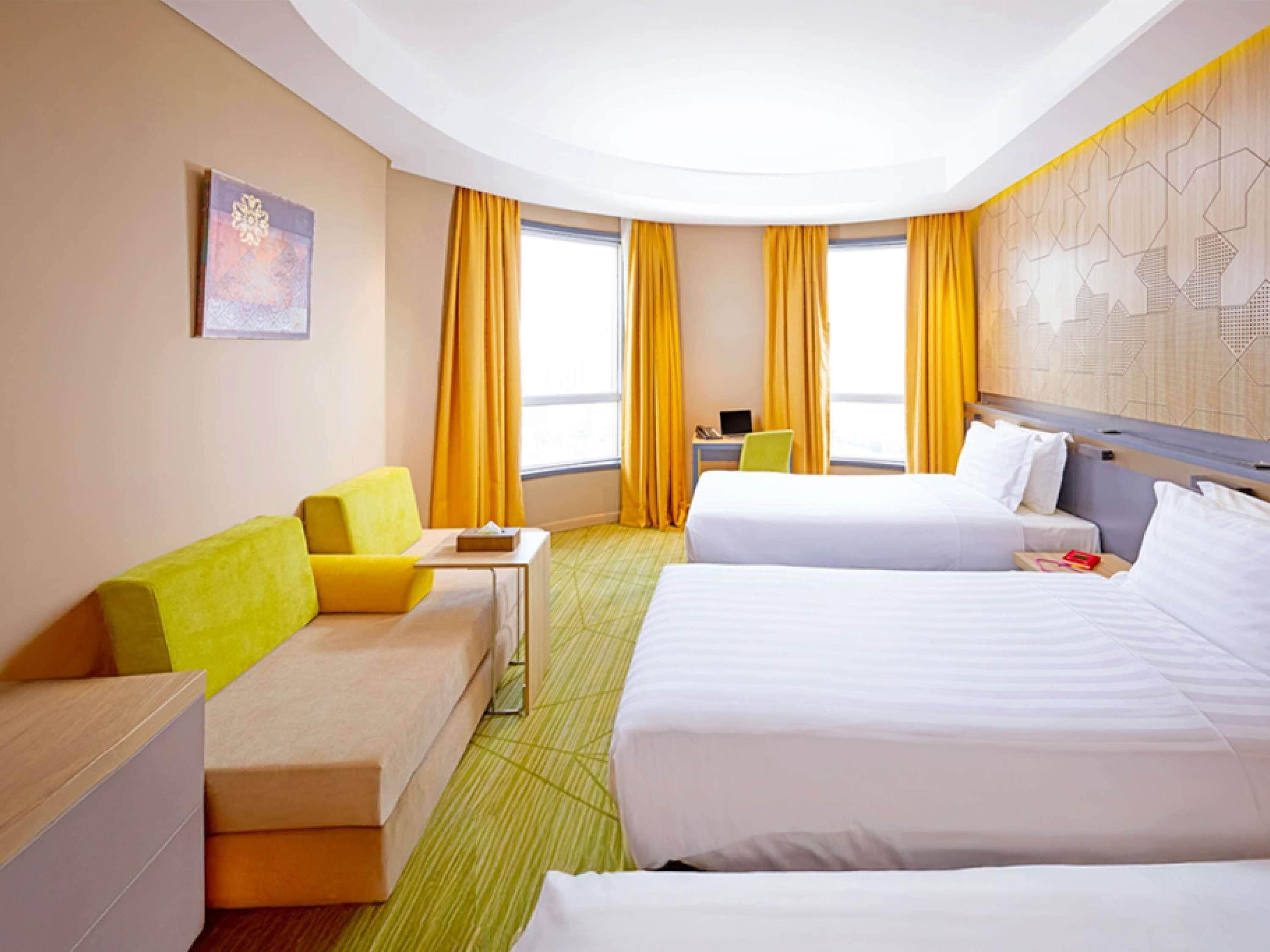 A hotel room with two beds, a sofa, a desk, and a window with curtains.