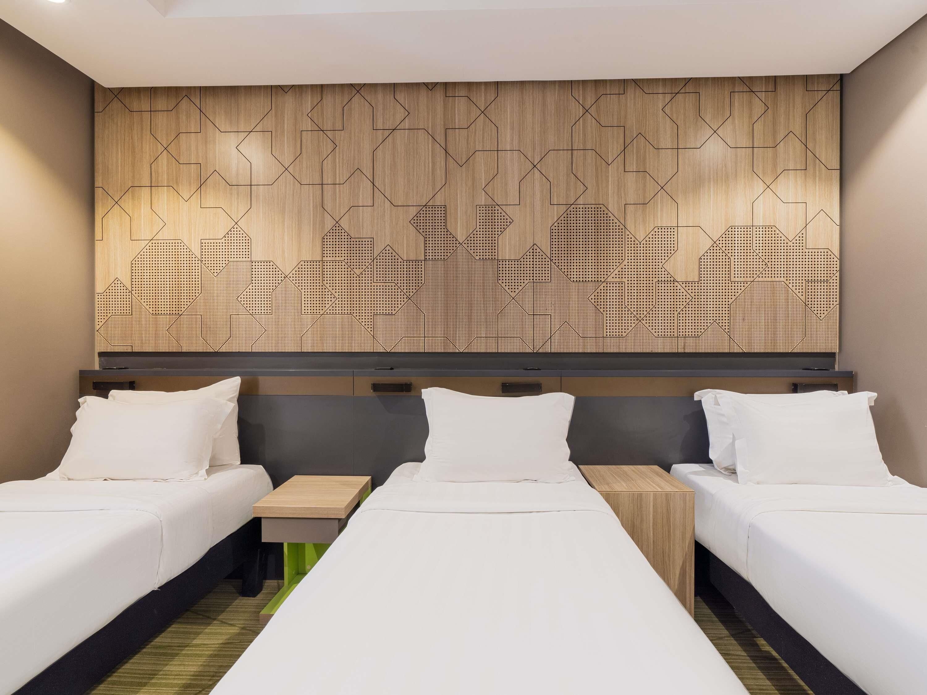 A hotel room with two beds, a wooden headboard with a geometric pattern, and a green accent wall.