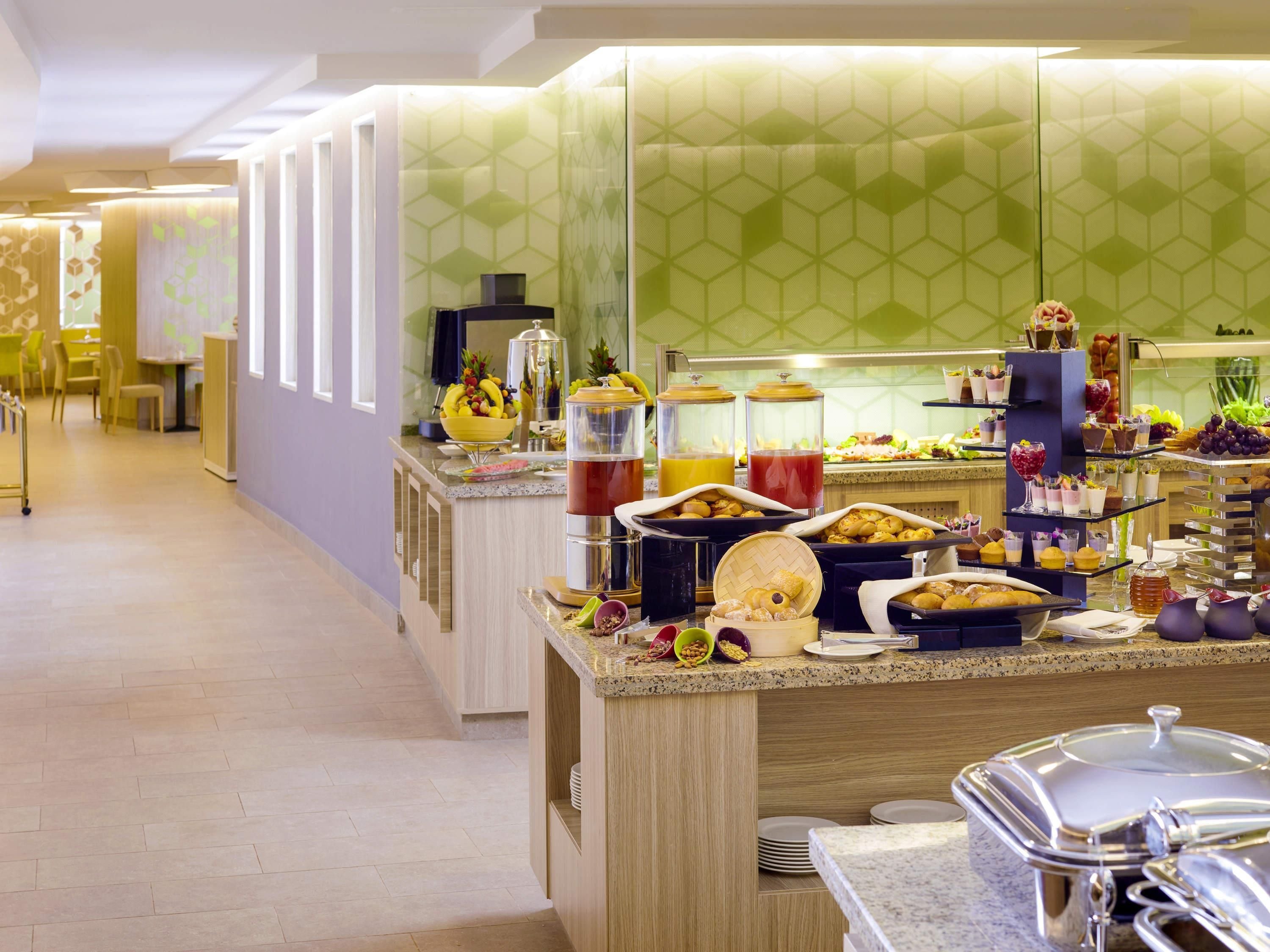 Ein Buffet mit verschiedenen Speisen und Getränken, eine Sitzecke mit Stühlen sowie eine Theke mit einer Kaffeemaschine.