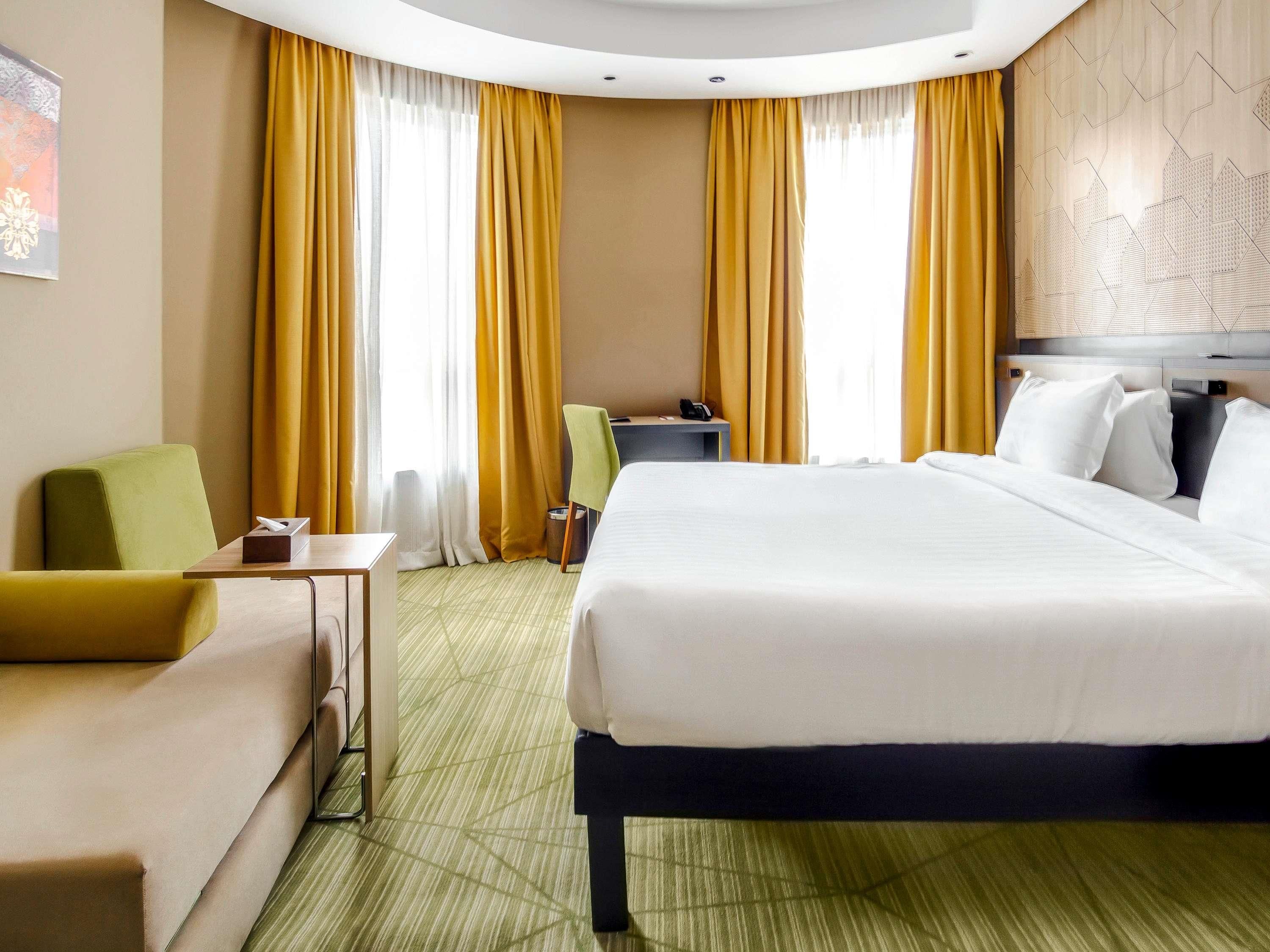 Quarto de hotel com cama, escrivaninha, cadeira e sofá.