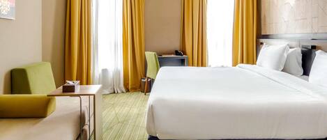 Quarto de hotel com cama, escrivaninha, cadeira e sofá.