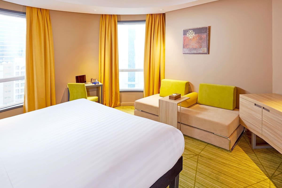 Una habitación de hotel con una cama grande, un sofá, un escritorio y un armario pequeño.