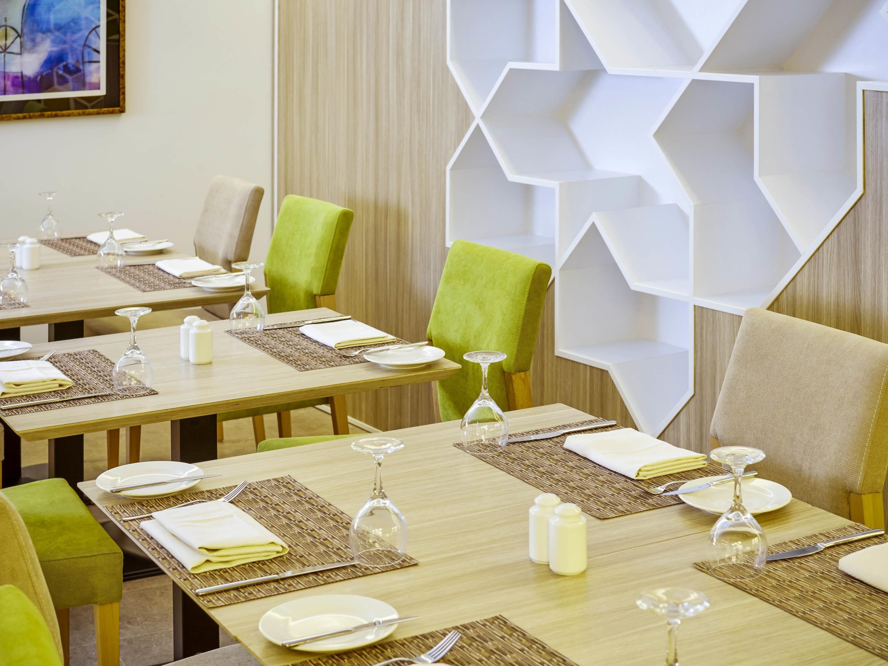 Un espace repas avec des tables dressées pour quatre personnes, chacune agrémentée d’un verre à vin, de couverts et de serviettes.