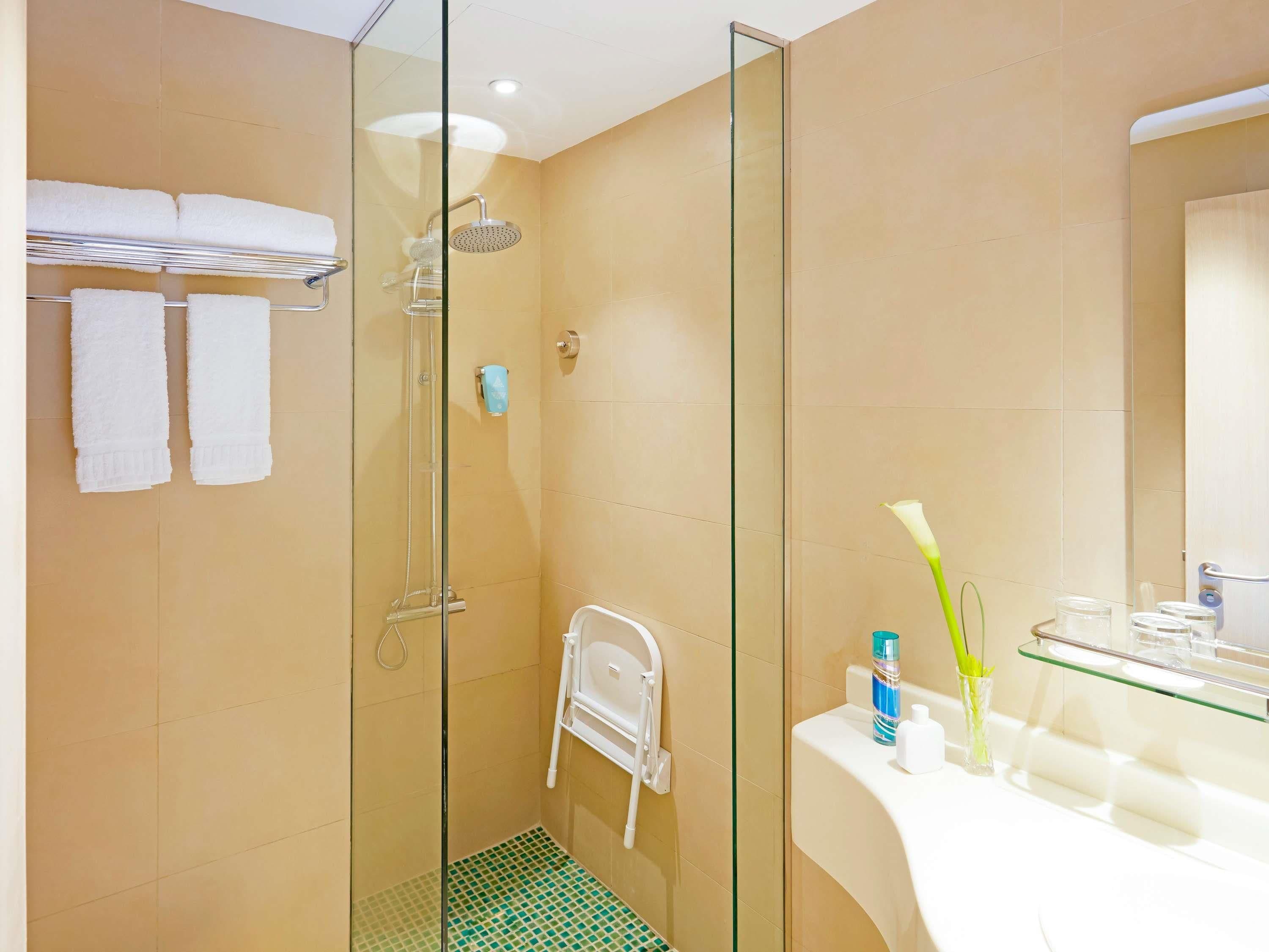 A modern bathroom with a glass-enclosed shower, a white towel rack, a glass shelf with toiletries, and a mirror.