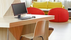 A modern office space with a wooden desk, a chair, a computer, and a bright yellow sofa in the background. - ibis Styles Makkah (Makkah)