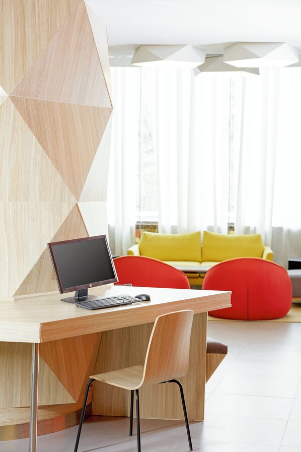 A modern office space with a wooden desk, a chair, a computer, and a bright yellow sofa in the background. - ibis Styles Makkah (Makkah)