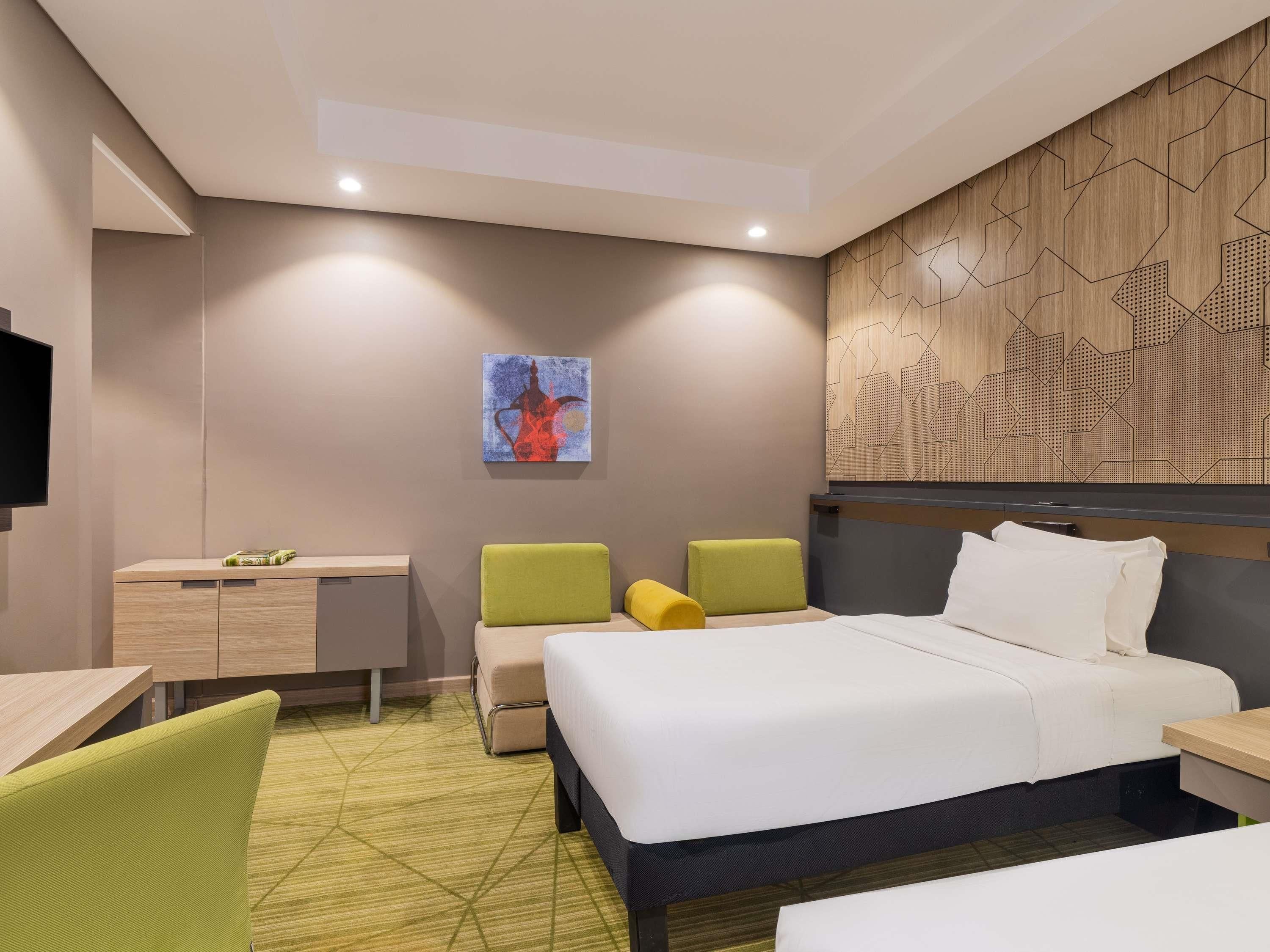 A modern hotel room with a bed, a desk, a chair, and a television.