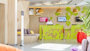 A modern reception area with a green desk, a receptionist, and a TV screen. - ibis Styles Makkah (Makkah)