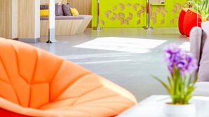 A modern interior with a sofa, a table with a vase of flowers, and a green wall with geometric patterns. - ibis Styles Makkah (Makkah)