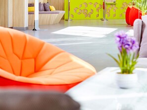 A modern interior with a sofa, a table with a vase of flowers, and a green wall with geometric patterns. - ibis Styles Makkah (Makkah)