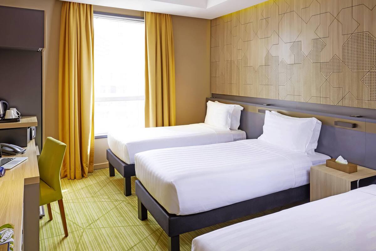 Une chambre d’hôtel avec deux lits, un bureau avec une chaise, un téléphone et une fenêtre avec des rideaux.