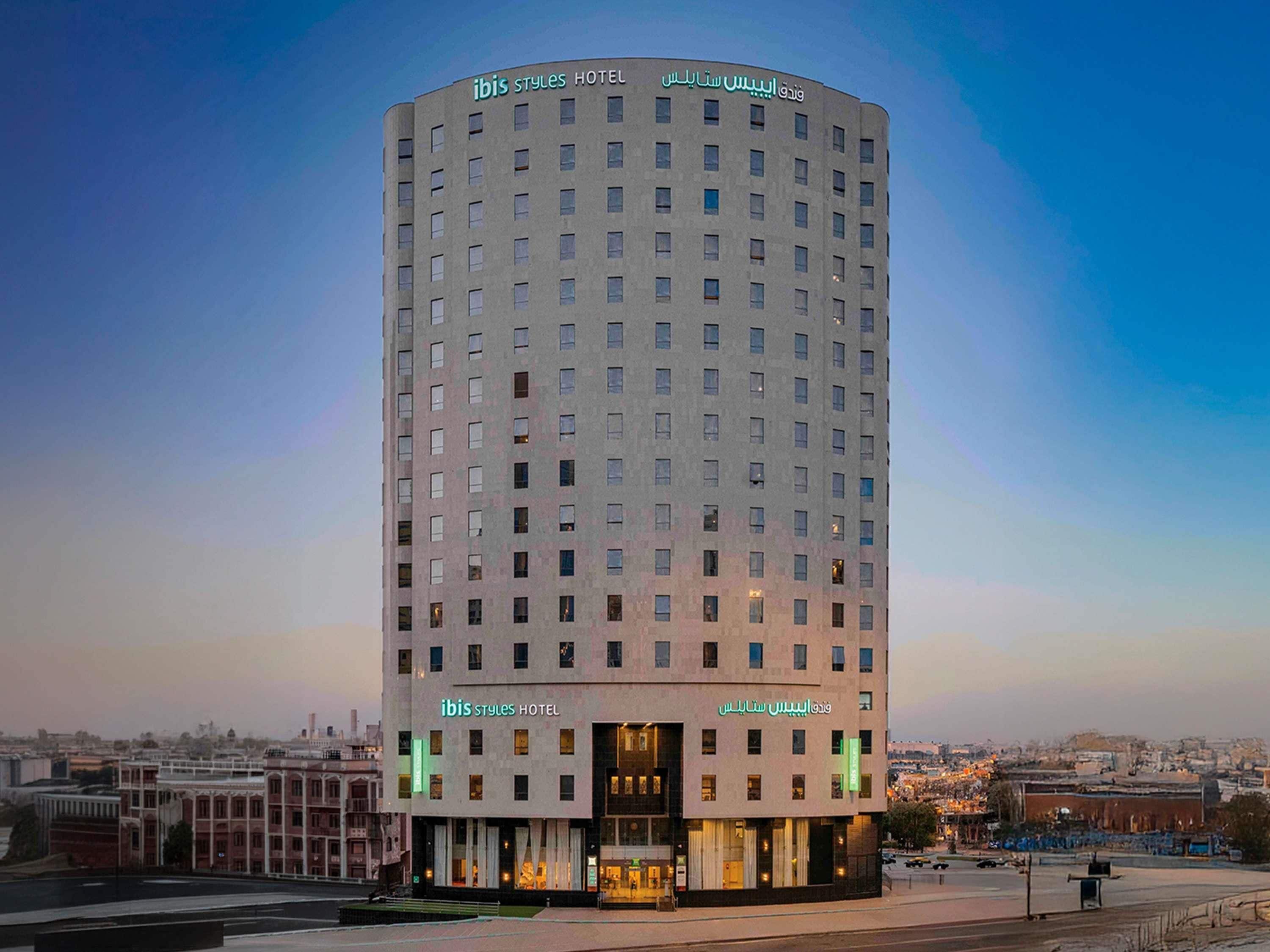 Un grand hôtel moderne à la façade incurvée, doté de nombreuses fenêtres et d’une signalétique en anglais et en arabe.