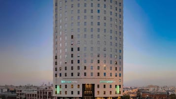 Un grand hôtel moderne à la façade incurvée, doté de nombreuses fenêtres et d’une signalétique en anglais et en arabe.