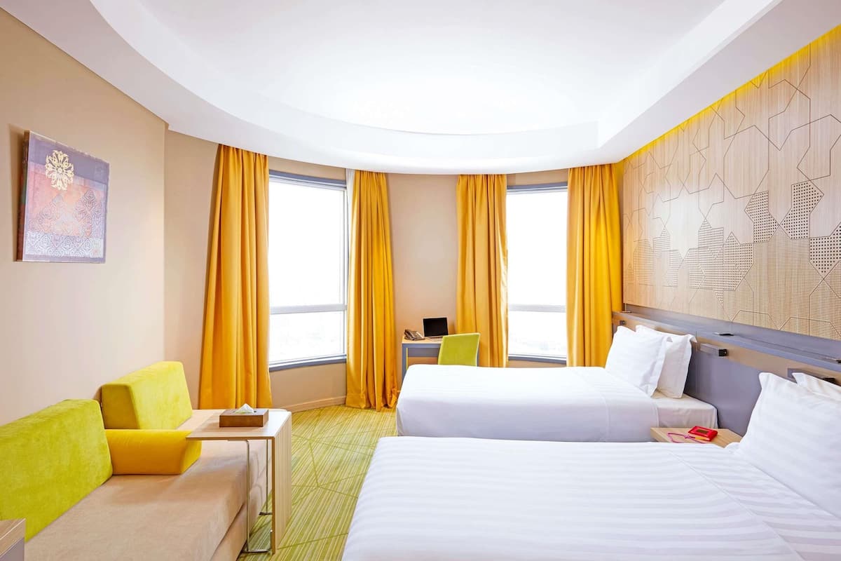 Habitación de hotel con dos camas, un escritorio, una silla y una ventana con cortinas.