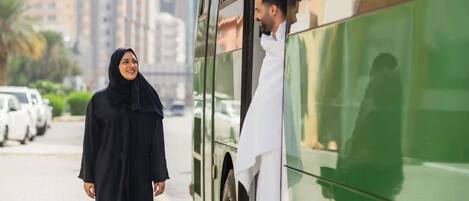 A person in a black dress standing next to a green bus.