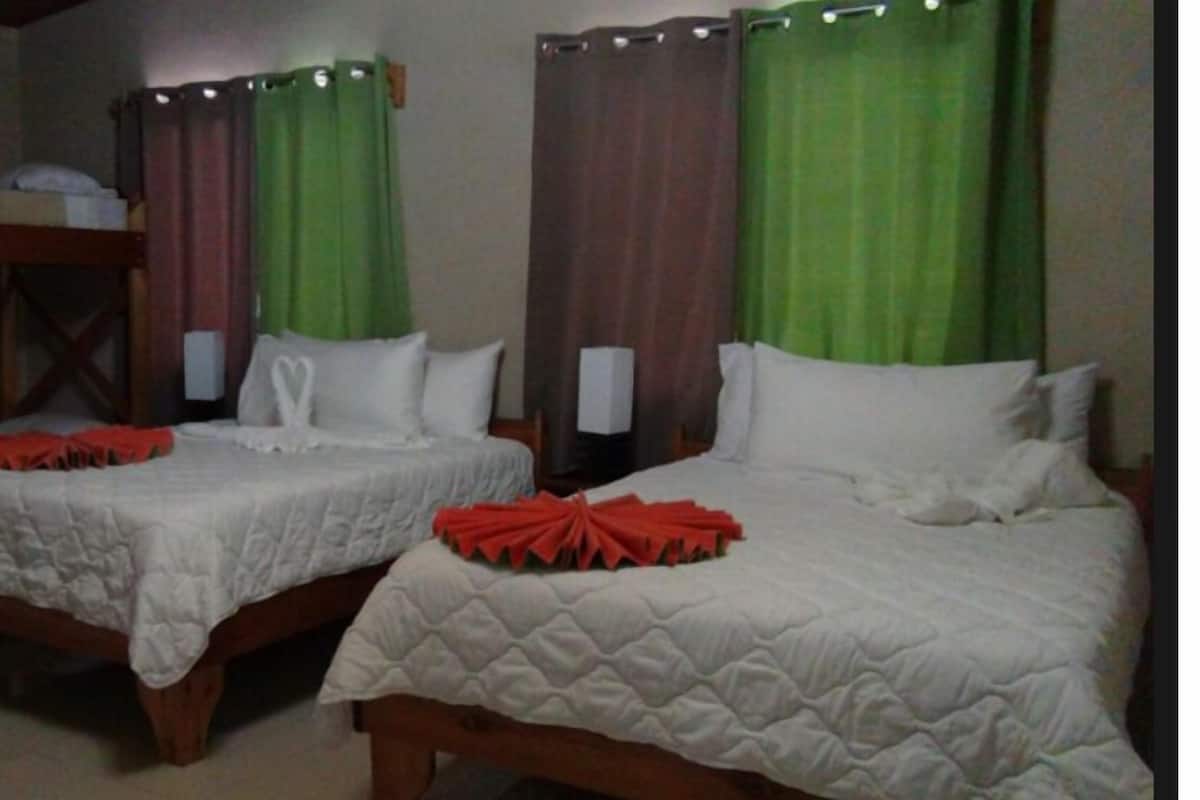 Two single beds with white bedding and red decorative pillows, green curtains, and bedside lamps in a hotel room.