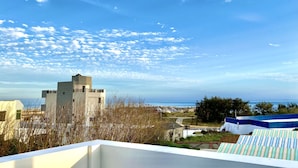 Una azotea con vistas al mar, un edificio de diseño singular y un cielo azul despejado.