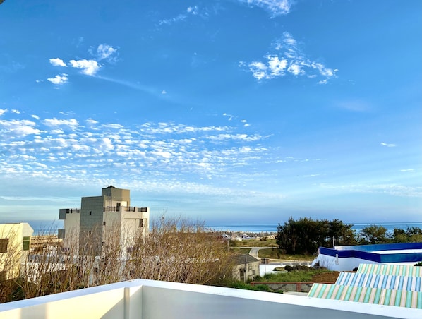A rooftop with a view of the sea, a building with a unique design, and a clear blue sky.