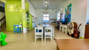 Una habitación luminosa y colorida con una pared verde que dice "BAY HOUSE", una mesa de madera, sillas, un jukebox y una guitarra.