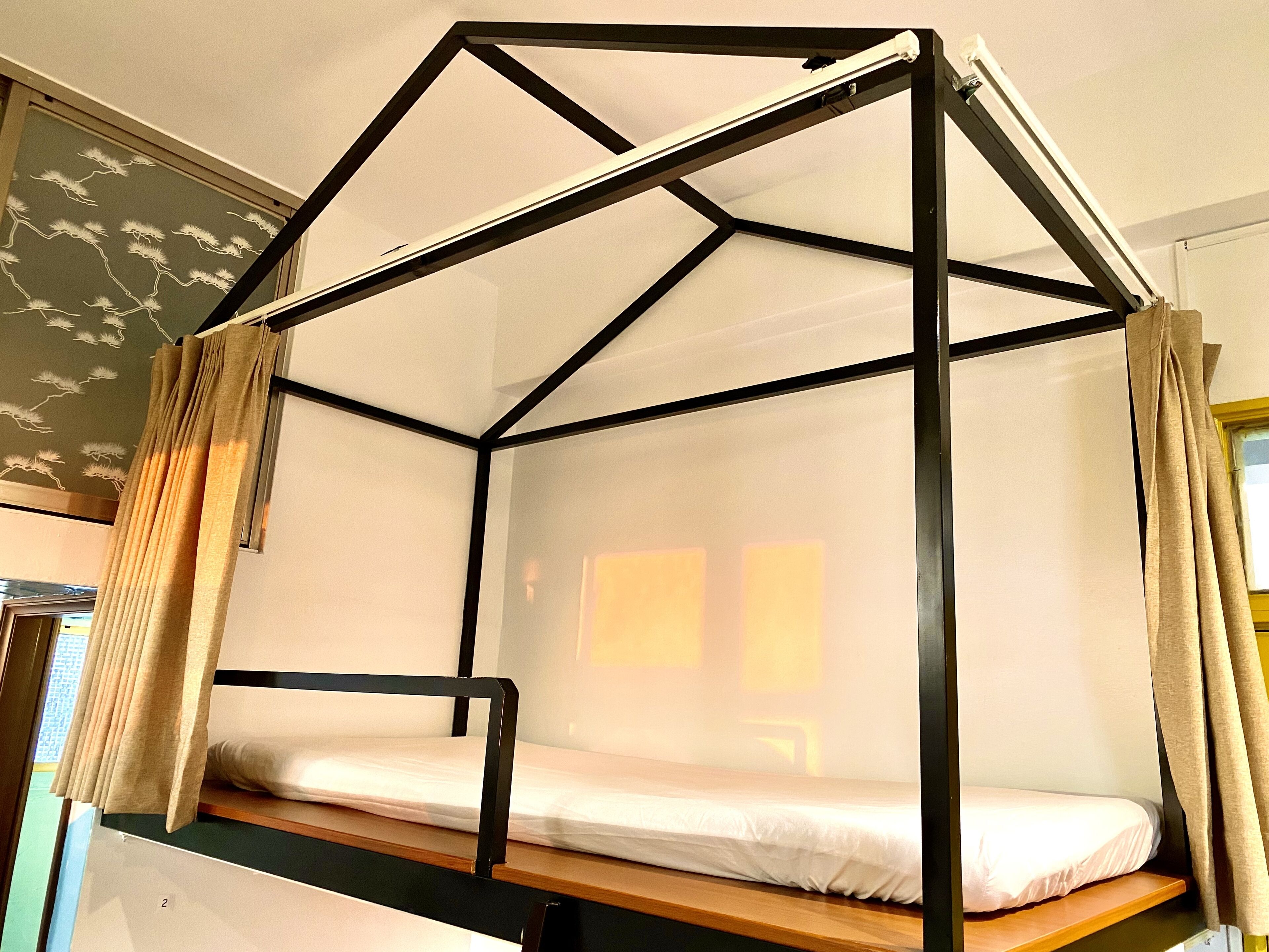 A bunk bed with a black metal frame and white bedding, curtains on both sides, and a wall with a decorative pattern.