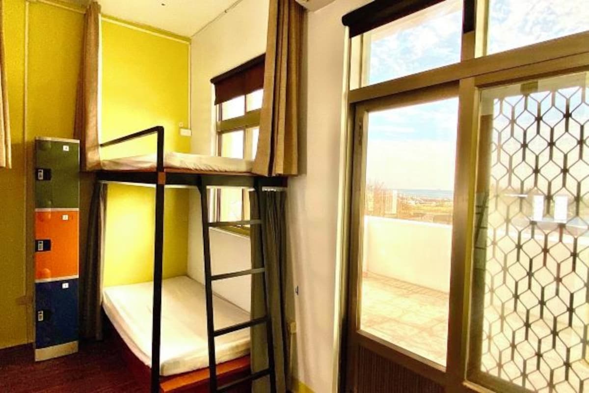 A dormitory room with bunk beds, a window with a view, and a door with a lock.