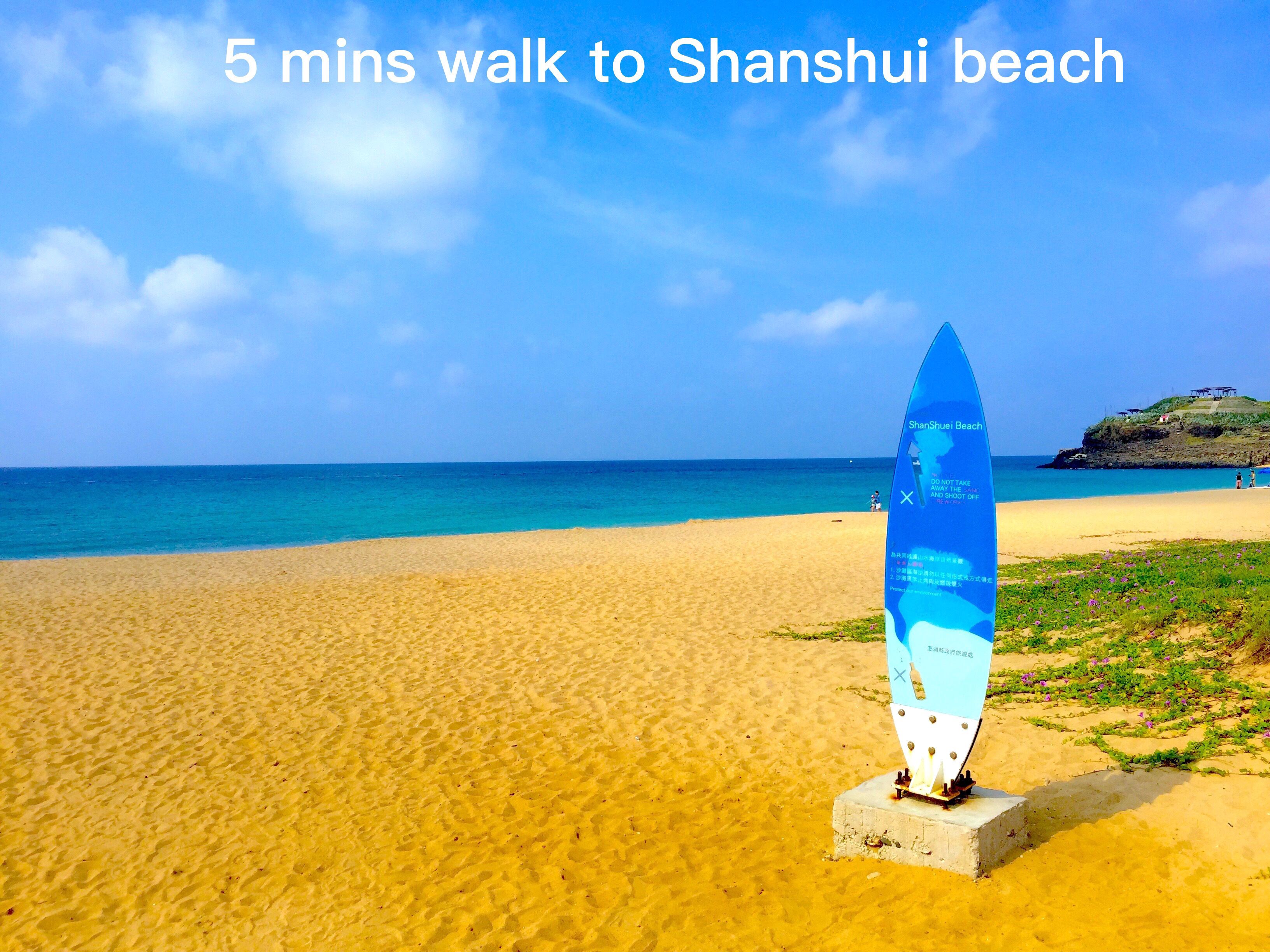 A beach with a surfboard-shaped sign indicating a 5-minute walk to Shanshui beach.