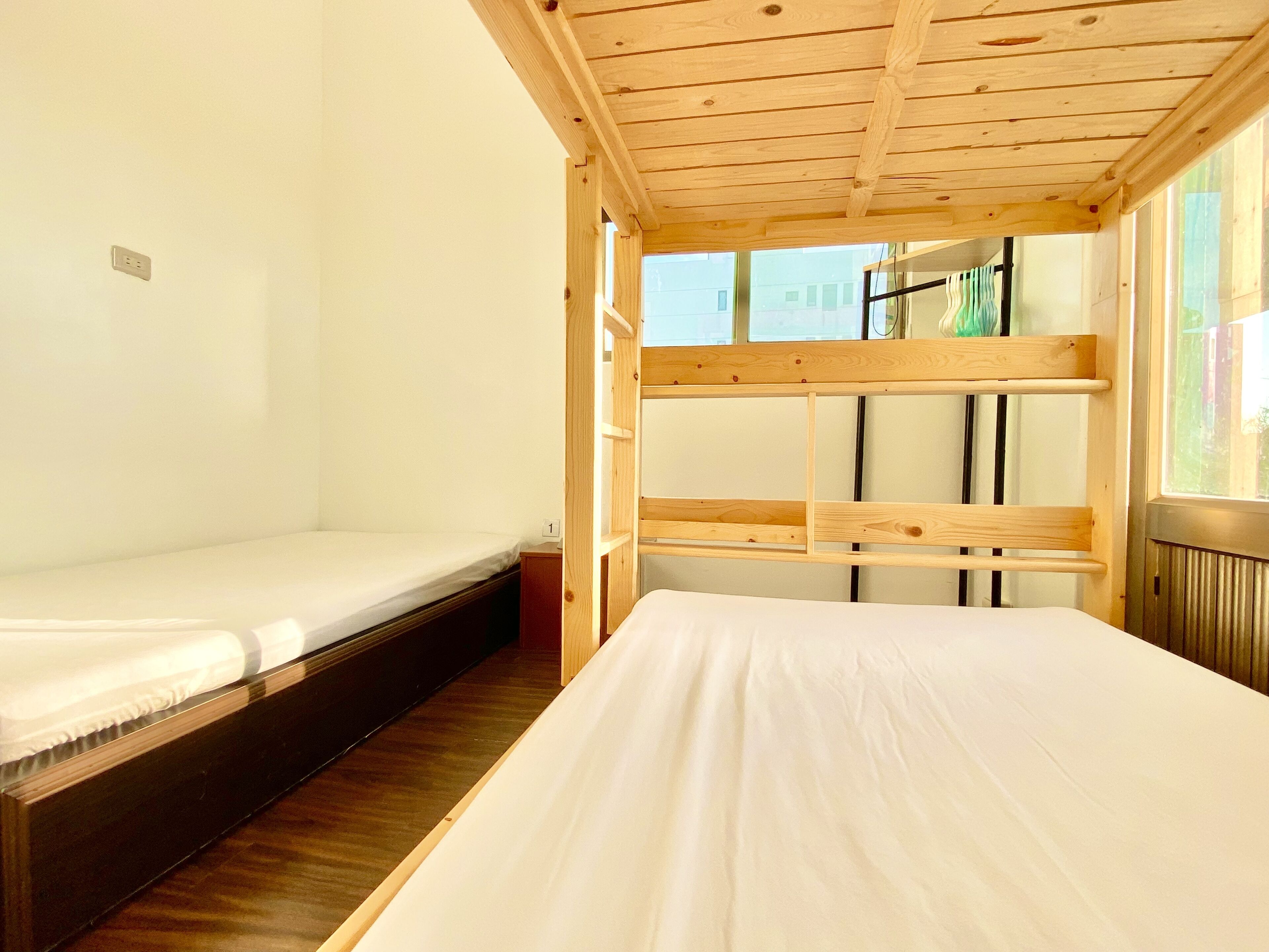 Une chambre avec deux lits superposés, un plafond en bois et une fenêtre donnant sur les bâtiments environnants.