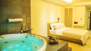 Een moderne hotelkamer met een ruim bad, een net opgemaakt bed en een schaal fruit op het nachtkastje.