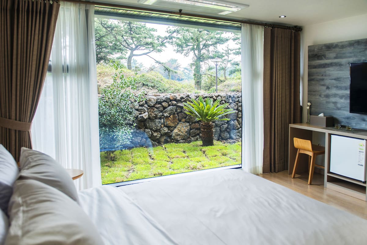 A bedroom with a large window, a bed, a desk, and a chair.