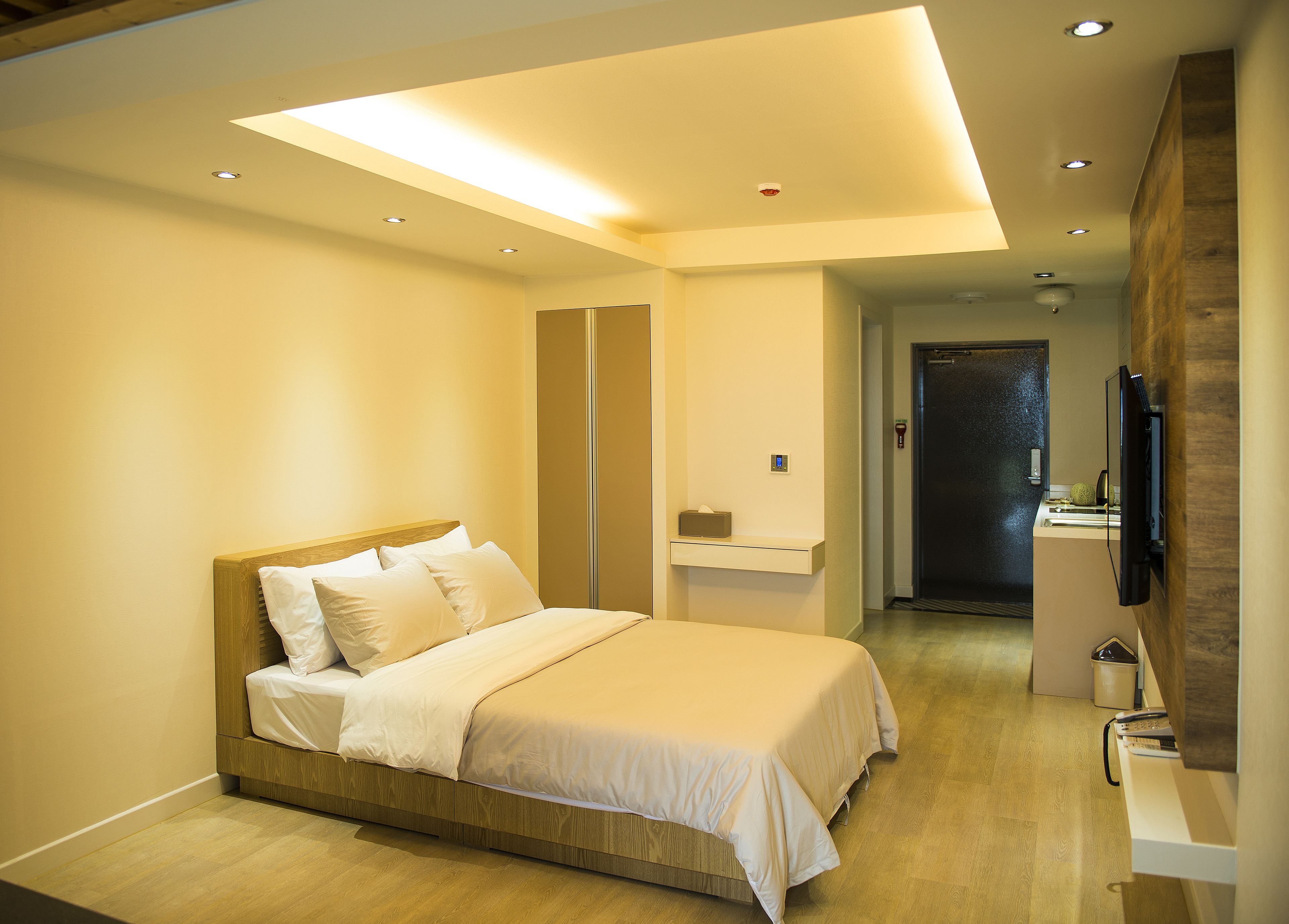 A modern bedroom with a wooden bed, a bedside table, a mirror, and a TV mounted on the wall.