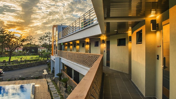 Een modern hotel met een balkon op de tweede verdieping, een zwembad en een aangelegde tuin.