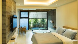 Een moderne slaapkamer met een groot bed, een zithoek met een tafel en stoelen, een badkuip en een aan de muur bevestigde televisie.