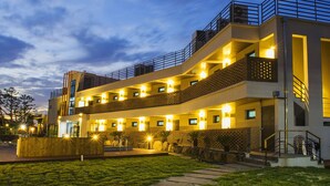 Een meerlaags hotel met een modern ontwerp, met balkons, buitenverlichting en een aangelegde tuin.