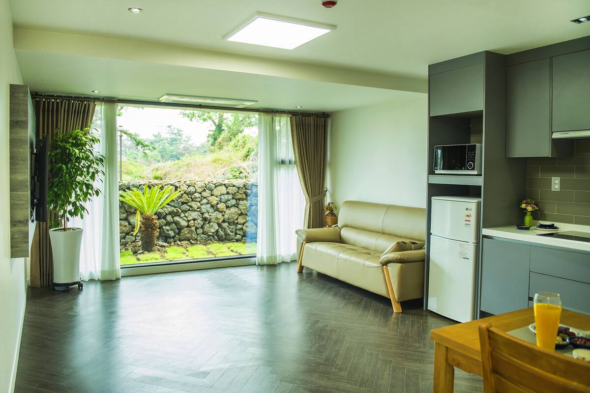 A modern living room with a sofa, a dining table with a glass of orange juice, and a kitchen area with a microwave.