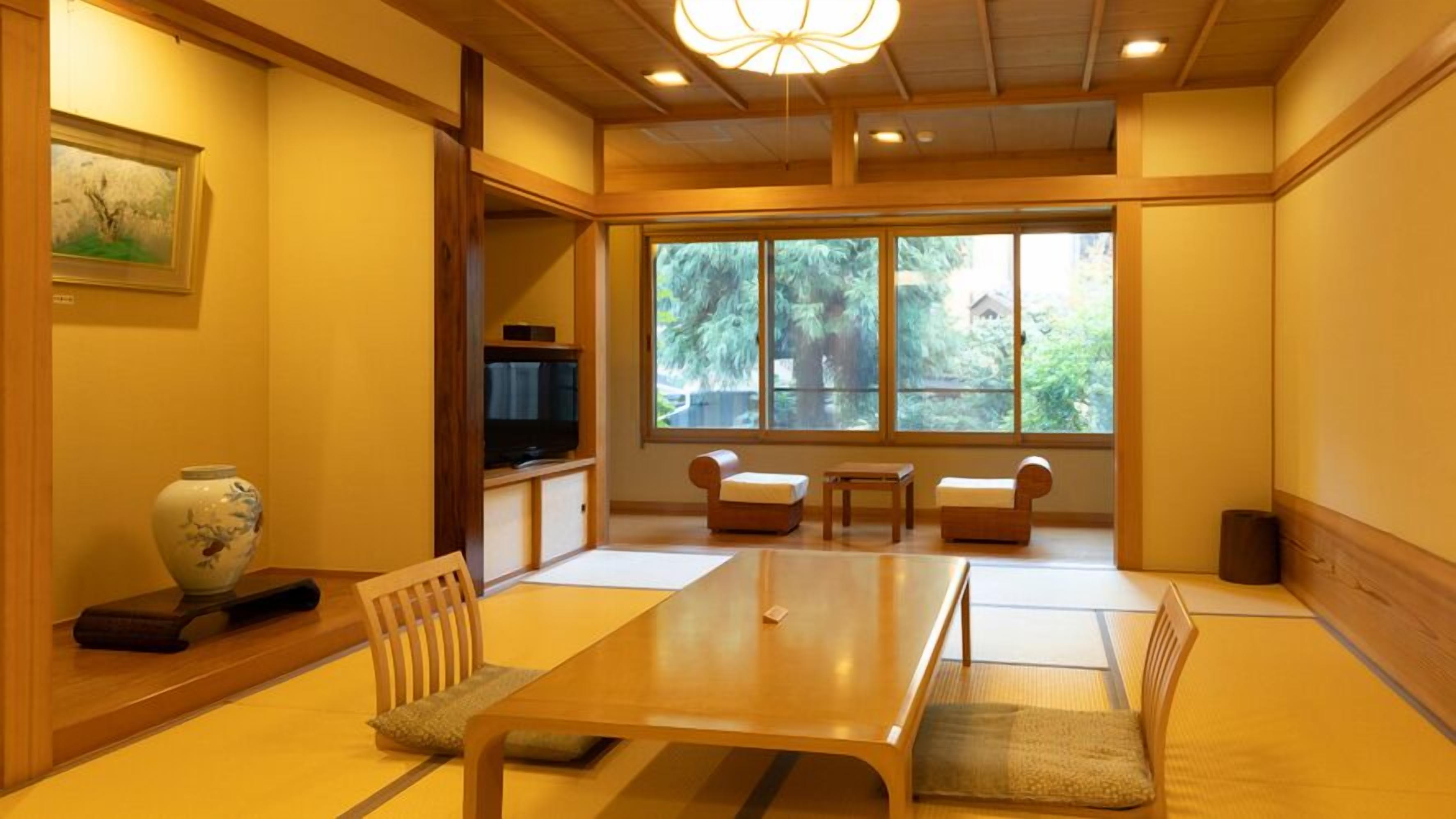 Quarto japonês tradicional com piso de tatame, mesa baixa, almofadas, televisão e uma grande janela com vista para árvores.