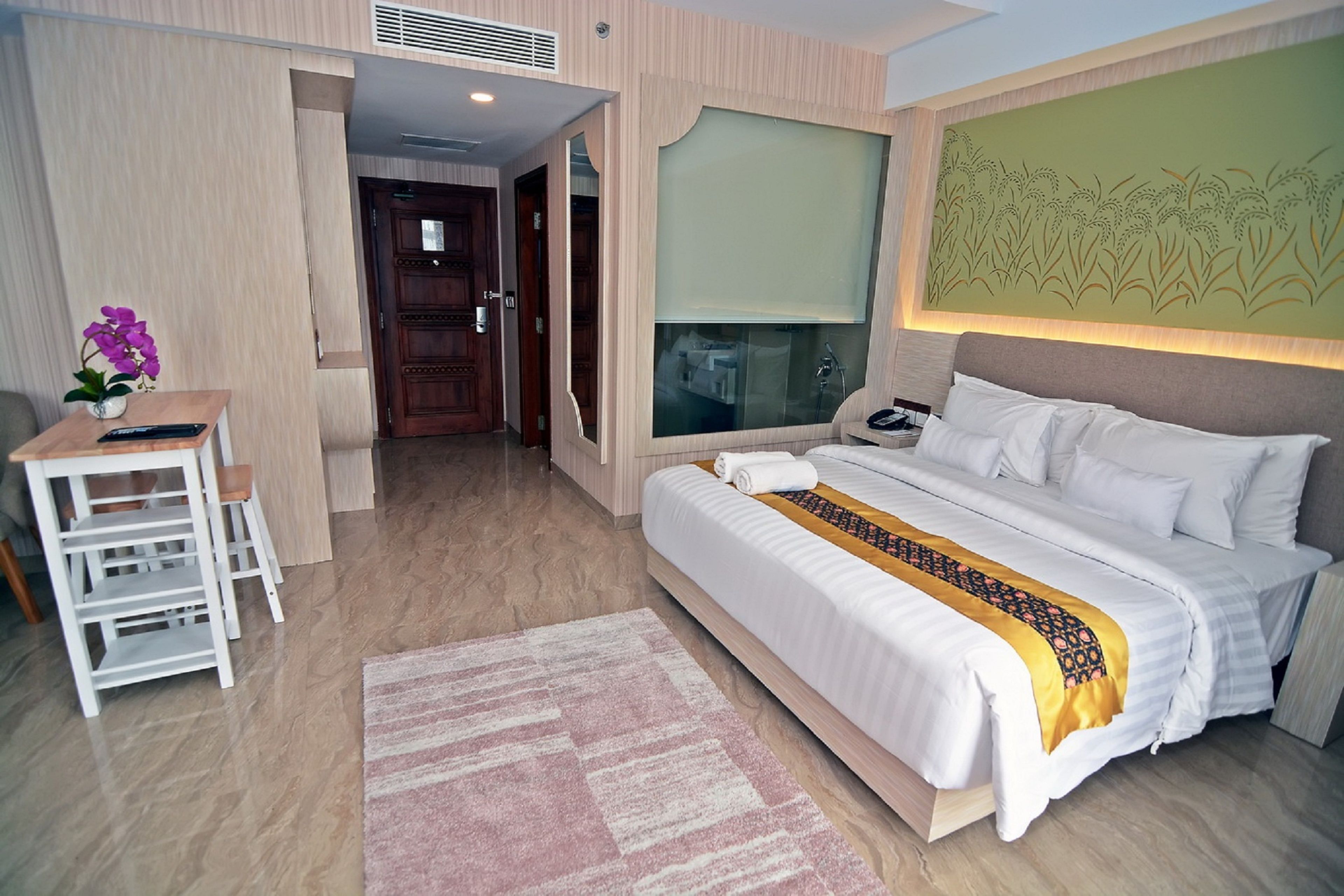 Habitación de hotel con una cama grande, un escritorio con silla, una mesita con un jarrón de flores y un ventanal con vistas al exterior.