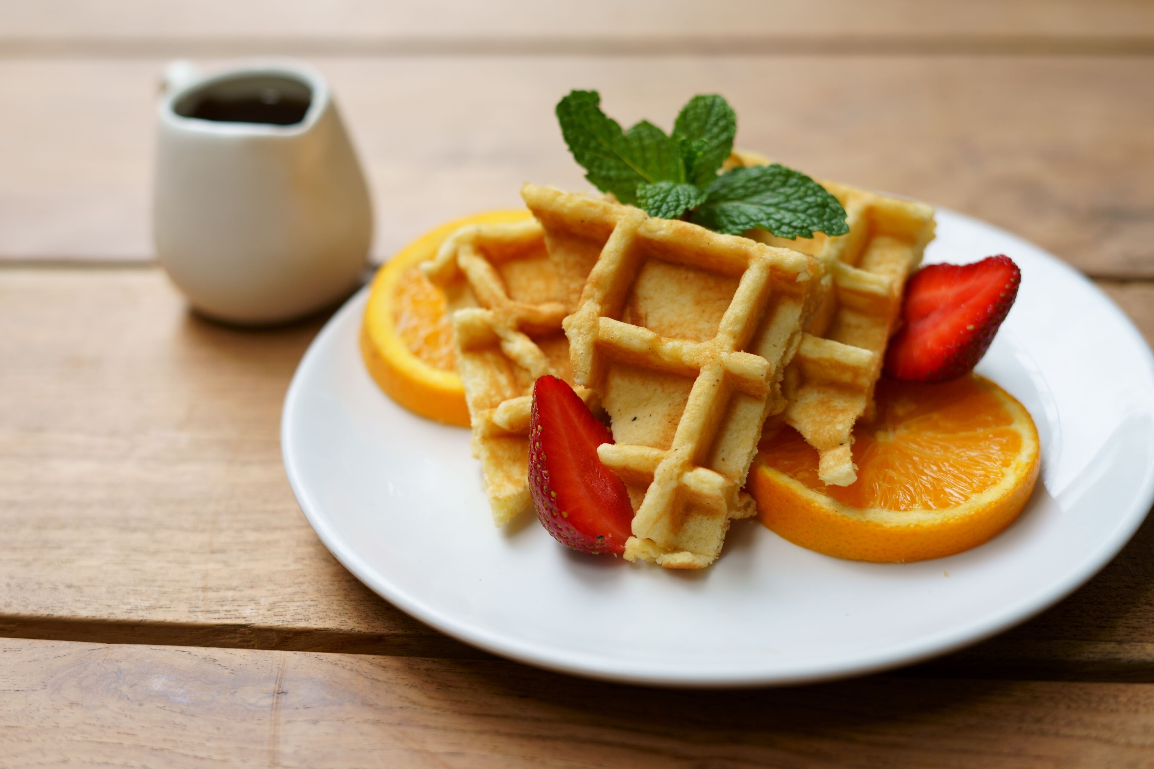 A plate with waffles, strawberries, and orange slices on a wooden table.