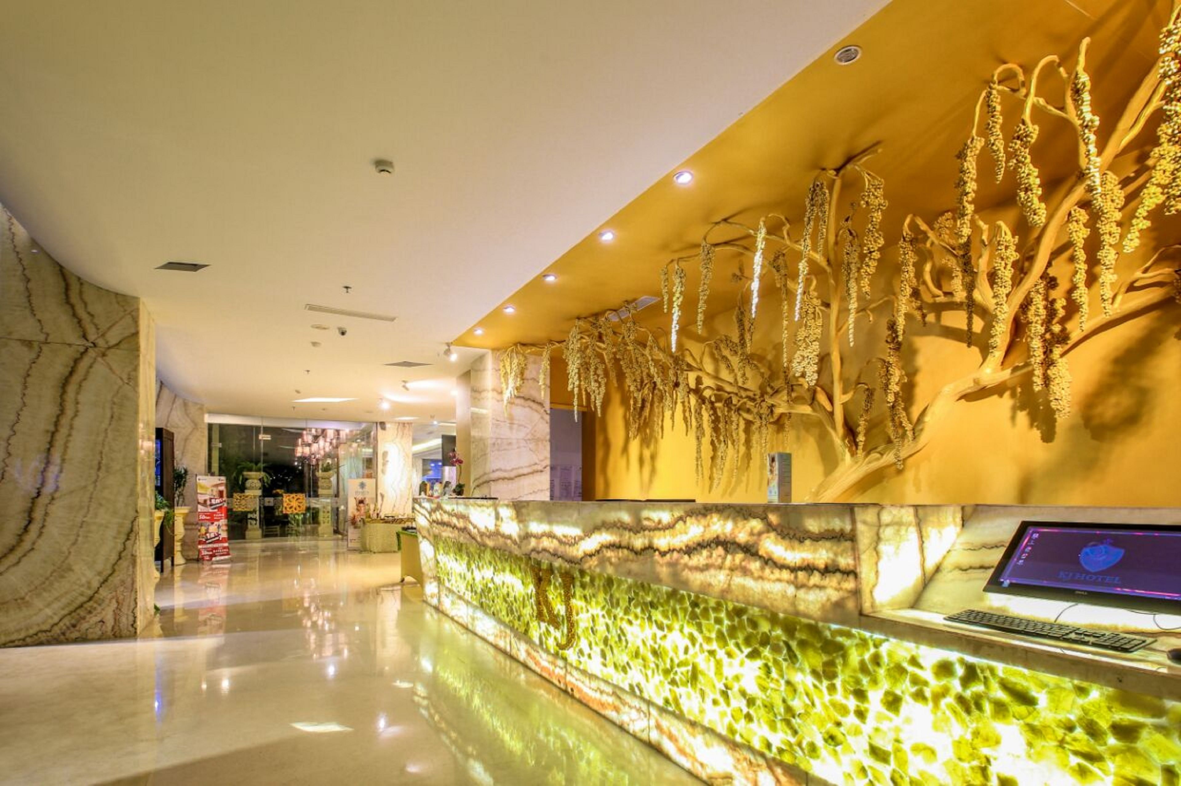 A modern hotel lobby with a marble reception desk, a wall-mounted computer, and a decorative plant display.