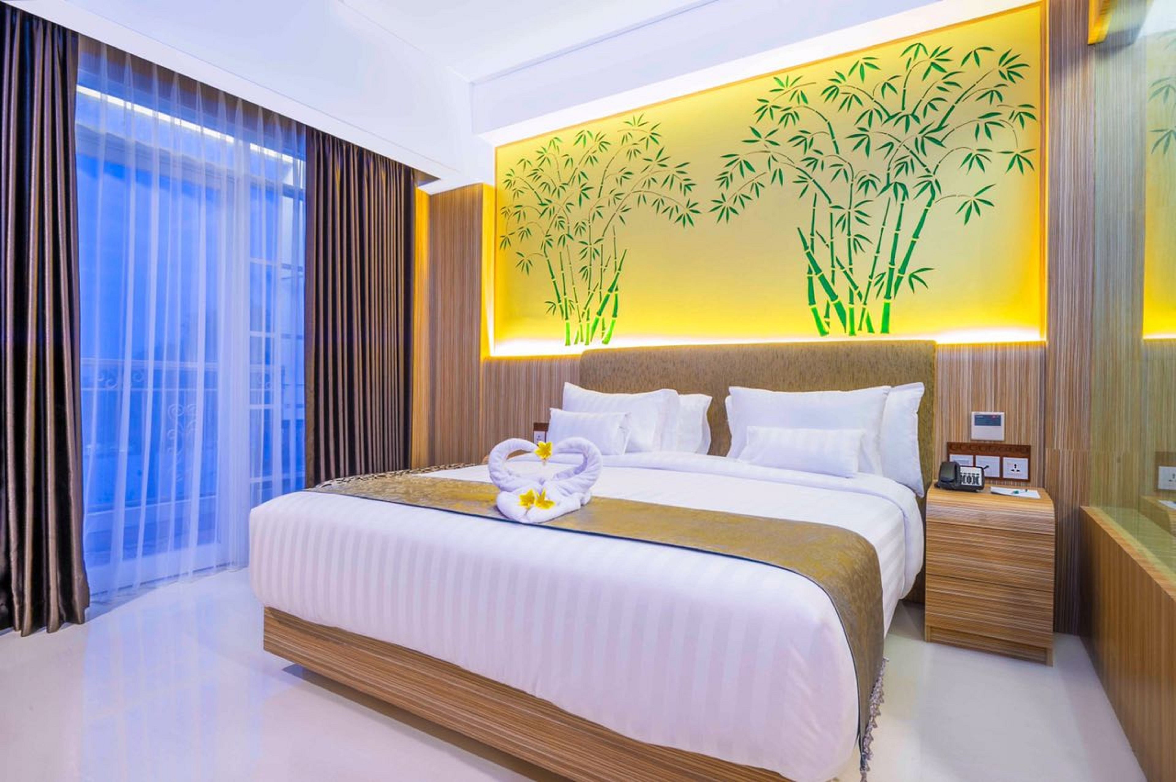 A hotel room with a large bed, a wall-mounted bamboo decoration, and a bedside table with a phone and a small lamp.