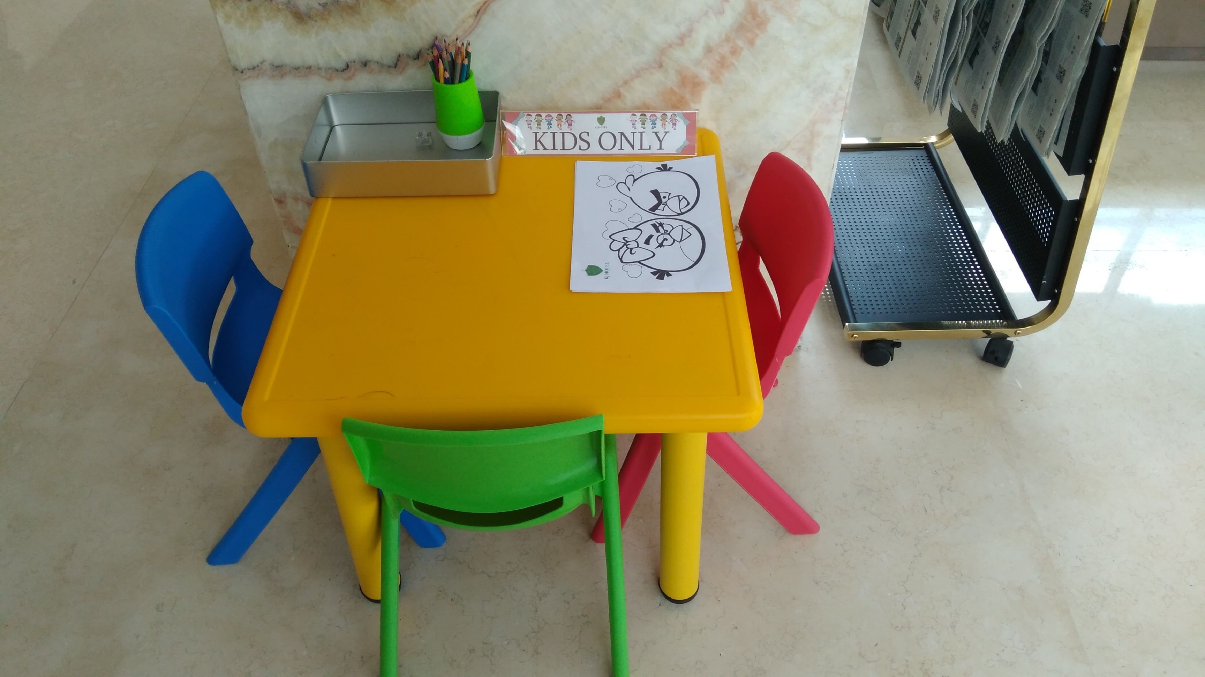 A children's table with a 'KIDS ONLY' sign, a drawing, and a green pencil holder.
