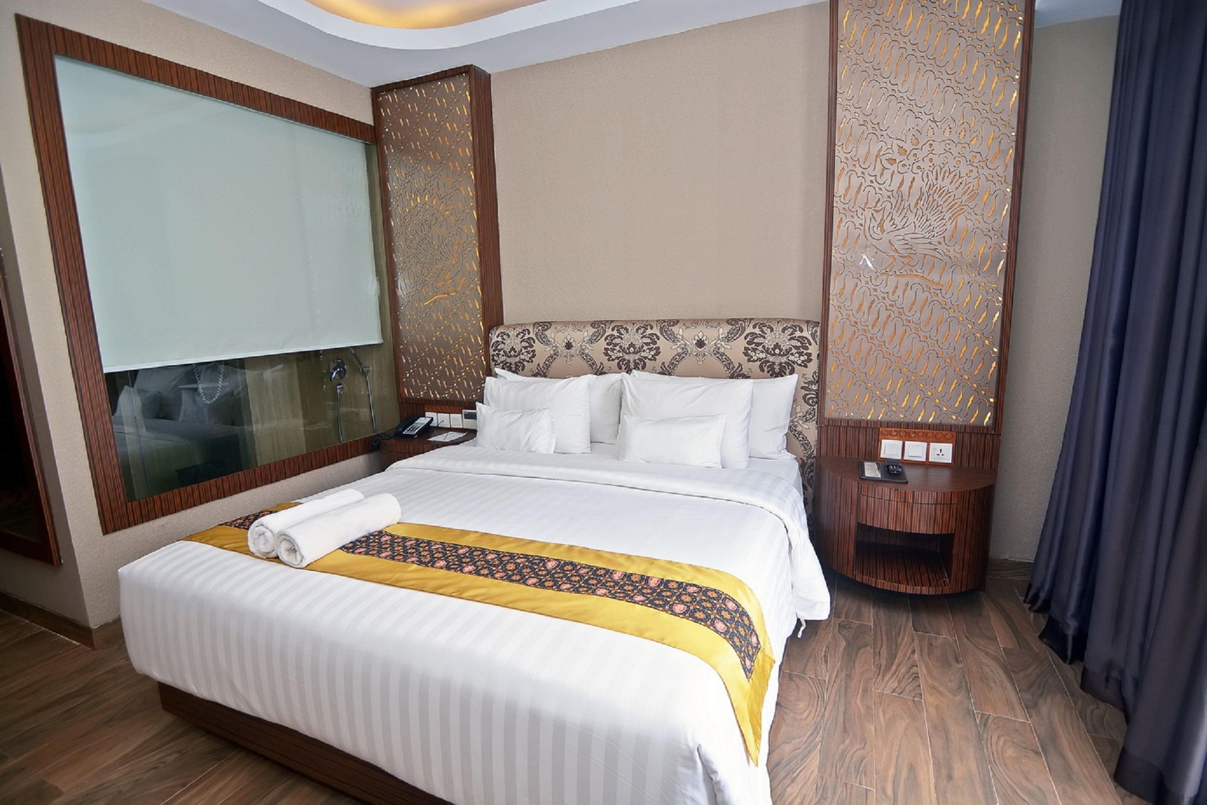 Habitación de hotel con una cama grande, una mesita de noche, un espejo y un separador decorativo.