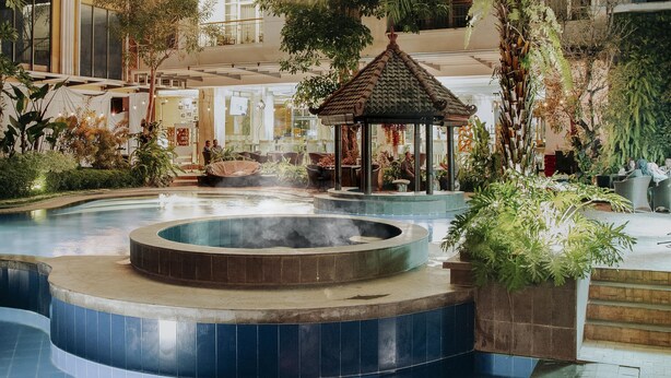 Uma área de fontes termais com um gazebo, cercada por vegetação exuberante e uma piscina.