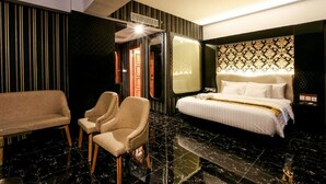 Quarto de hotel com uma cama, duas poltronas, um sofá, um espelho e parede estampada.