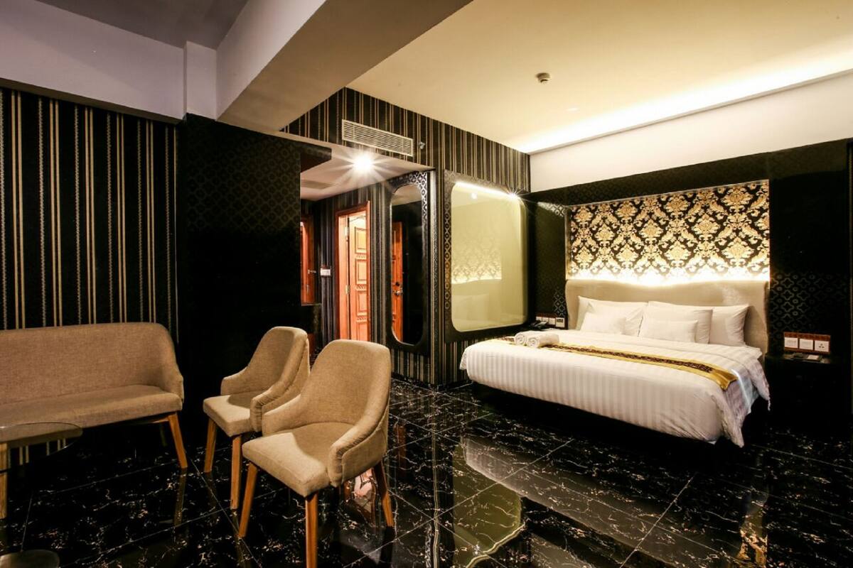 A hotel room with a bed, two armchairs, a sofa, a mirror, and a patterned wall.