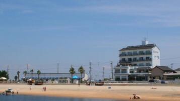 A coastal building with multiple floors, a sandy beach in the foreground, and calm water reflecting the structure.